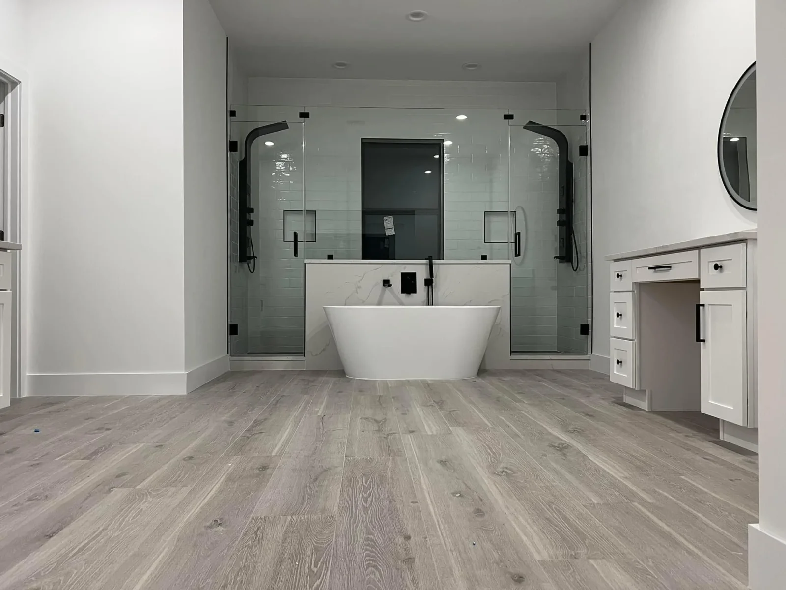 Luxury bathroom with freestanding tub, dual vanity, frameless glass shower, marble counters, and wood-look flooring