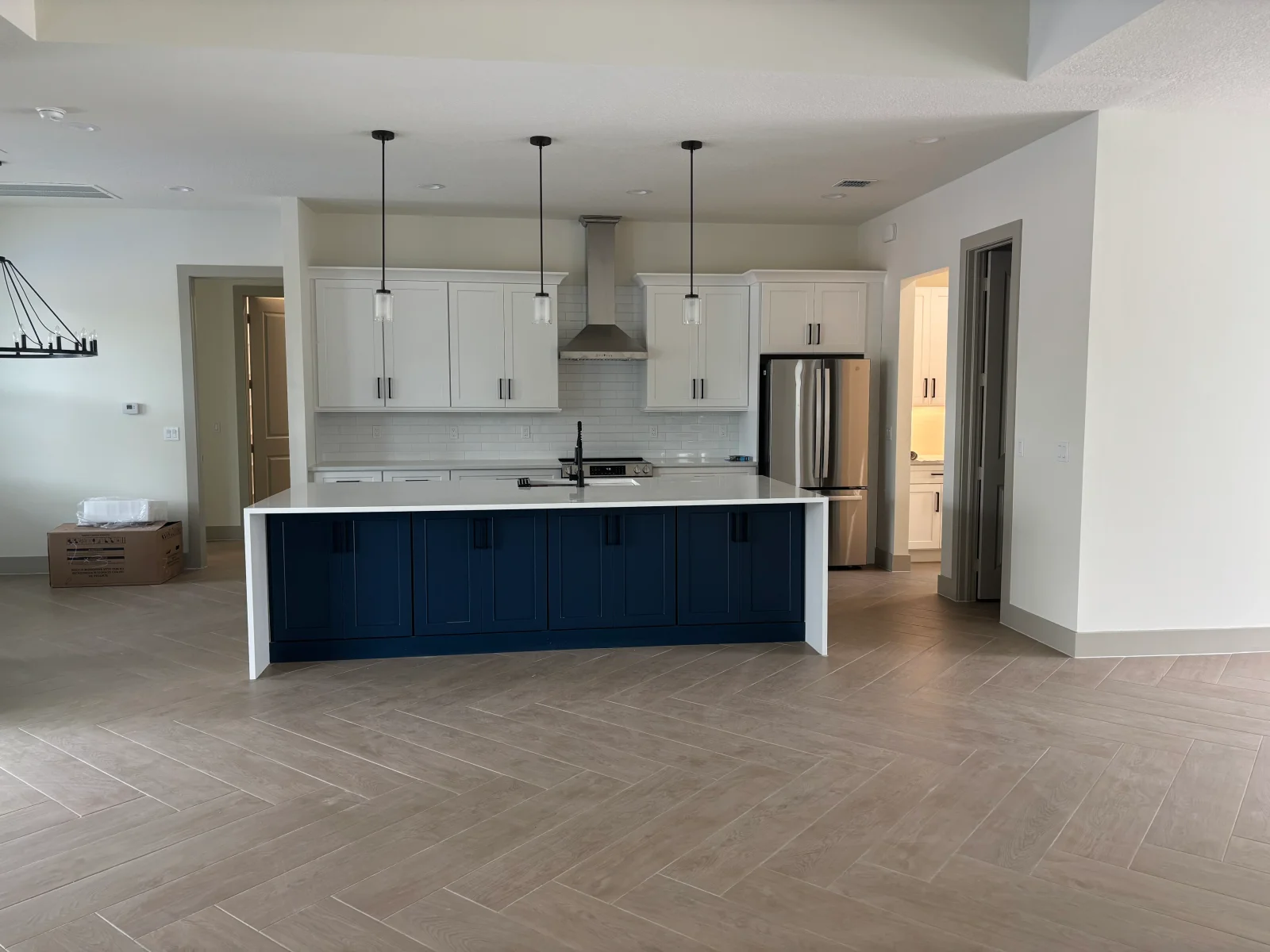 White and navy kitchen with island, stainless steel appliances, subway tile backsplash, pendant lights