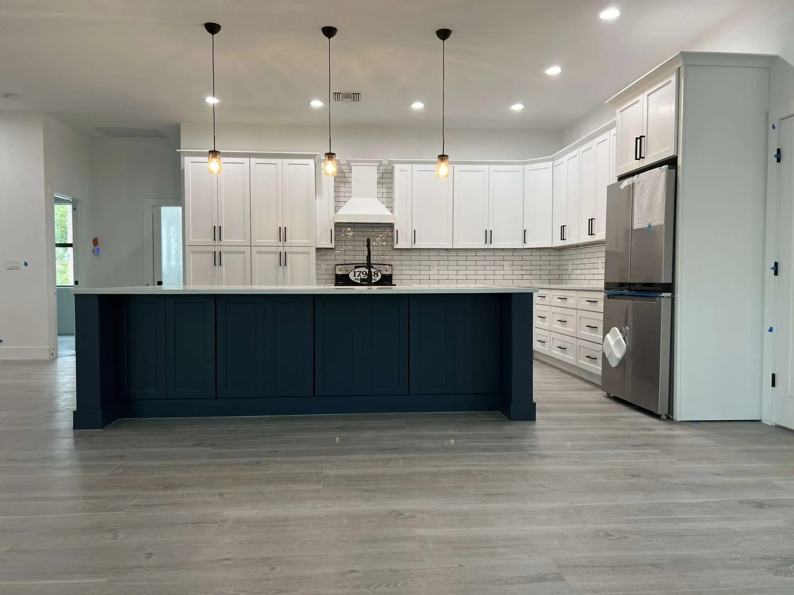 Two-tone kitchen with white cabinets, navy island, subway tile, stainless steel appliances, and pendant lights