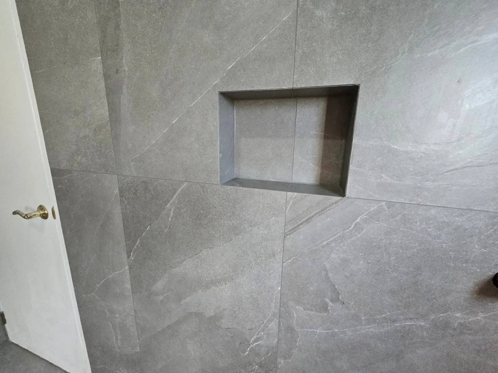 Gray large-format tile walls with recessed niche and brass hardware fixture