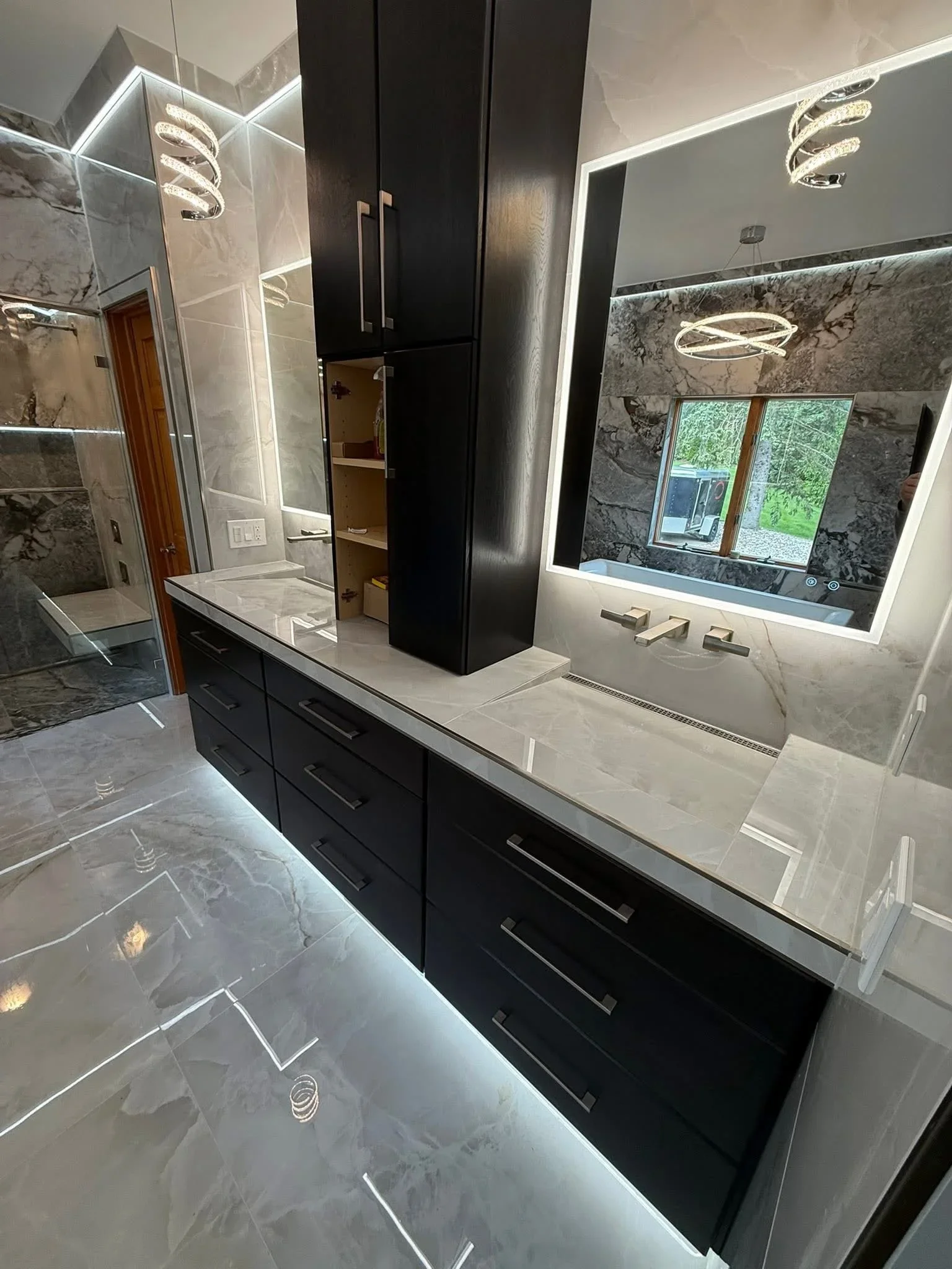 Dual-sink bathroom vanity with black cabinets, white quartz counters, marble tile walls, and frameless shower