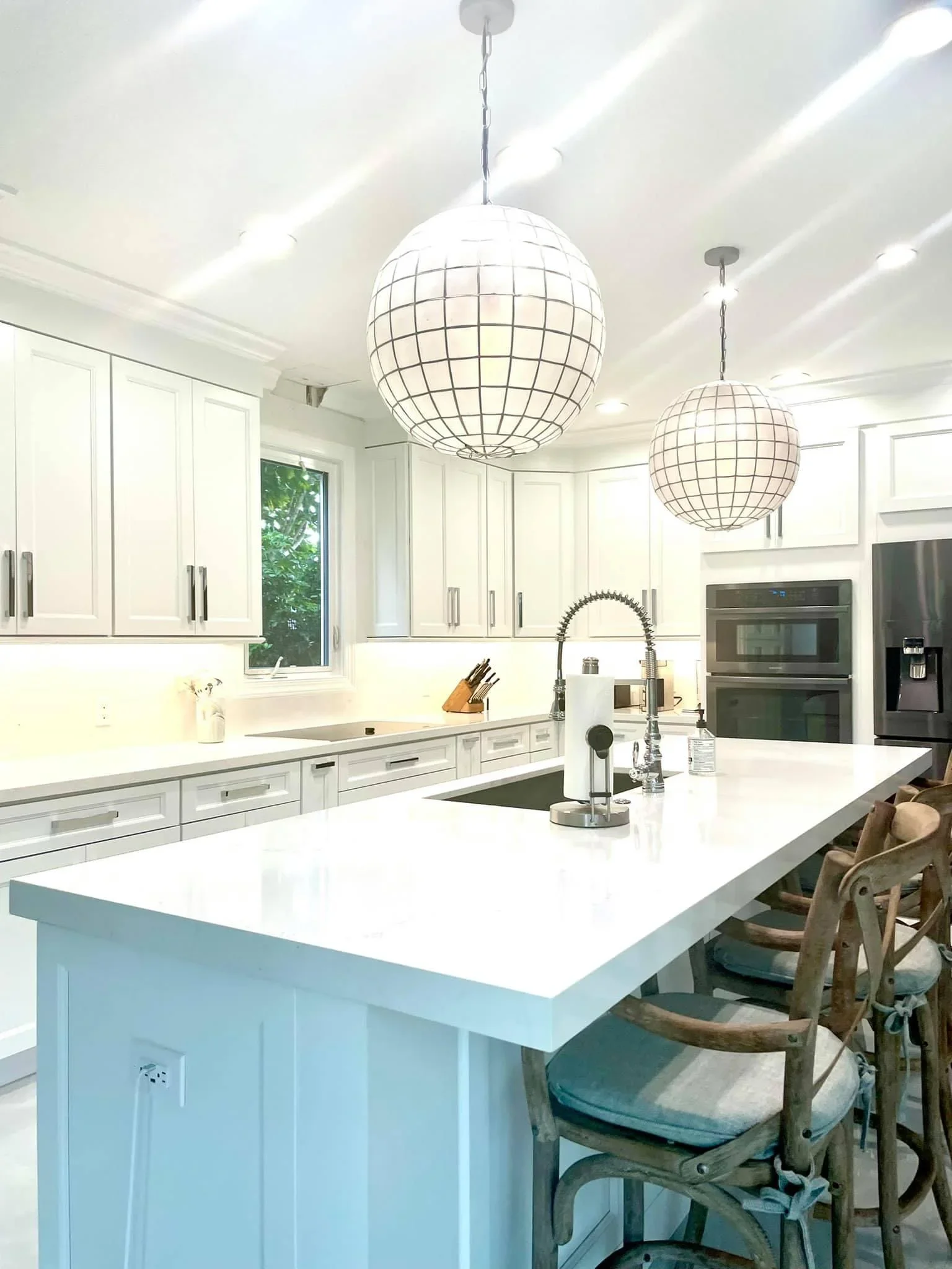 White kitchen with blue island, quartz counters, shaker cabinets, and globe pendant lights