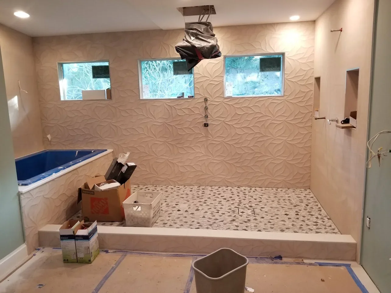 Bathroom shower with textured wall tile, glass enclosure, and mosaic floor tile during installation