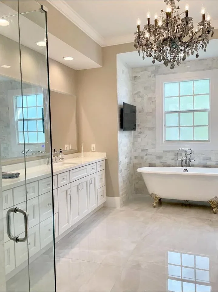Luxury bathroom with white vanity, marble tile, frameless shower, and freestanding tub