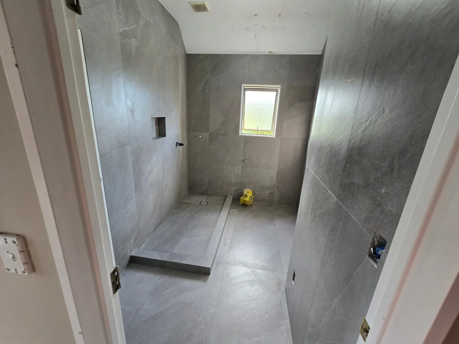 Gray tile bathroom with large-format tiles on walls and floor, integrated shower pan, and recessed niche