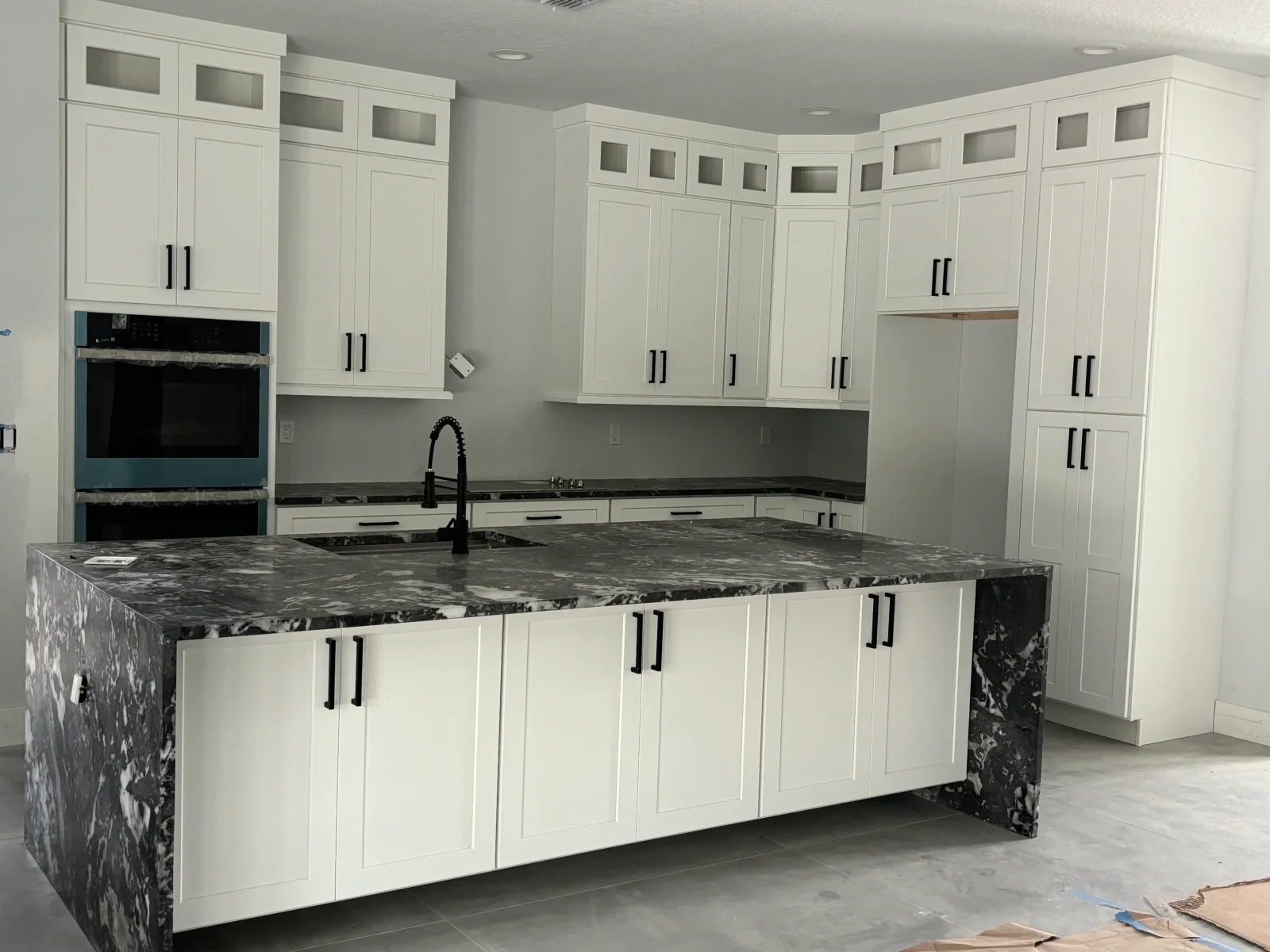 White shaker cabinets with black marble waterfall island, double wall ovens, and glass-front upper cabinetry