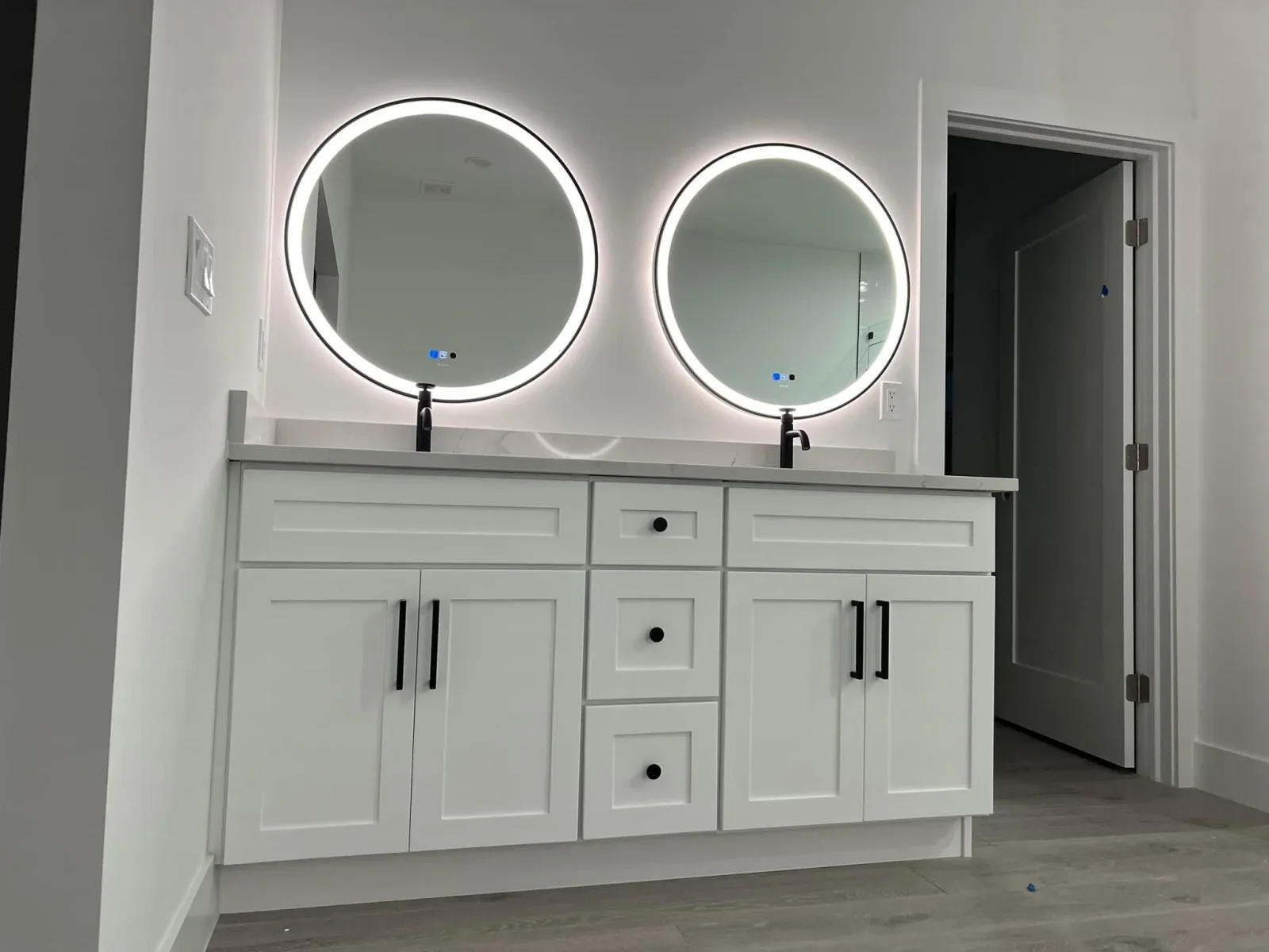 White shaker vanity with dual circular LED mirrors, black faucets, and quartz countertop