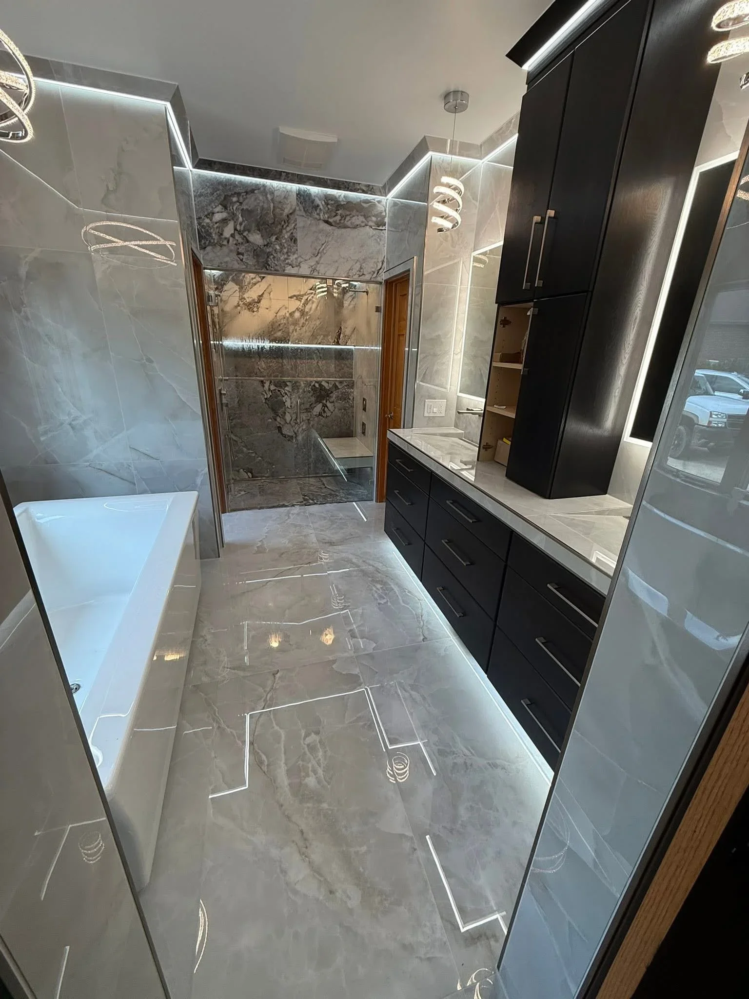 Marble tile bathroom with black cabinetry, frameless shower enclosure, and LED lighting