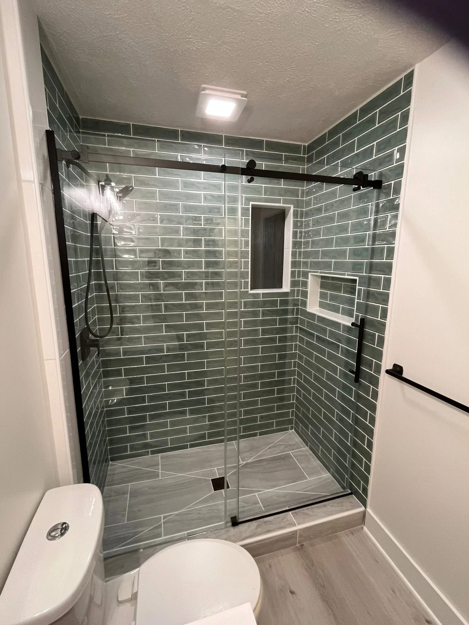 Bathroom shower with sage green subway tile walls, gray floor tile, and frameless glass enclosure
