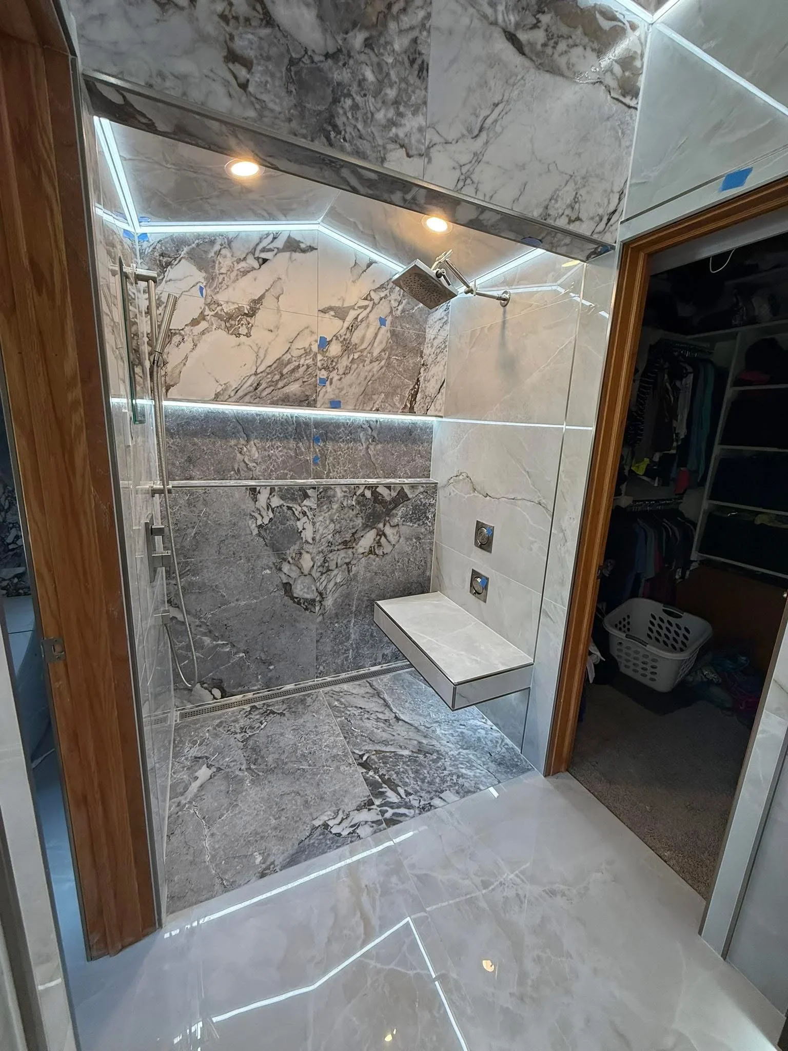 Marble tile shower with built-in bench, frameless glass doors, and LED lighting