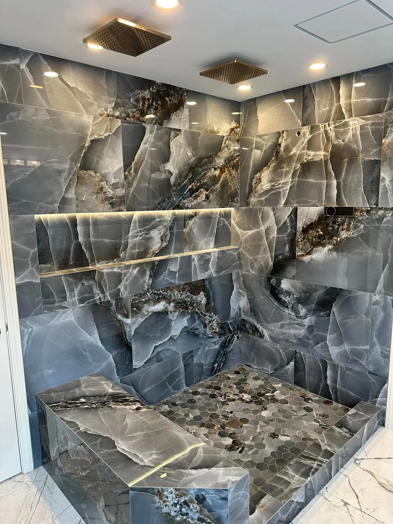 Marble tile shower with brass accents, hexagonal floor tiles, and recessed lighting