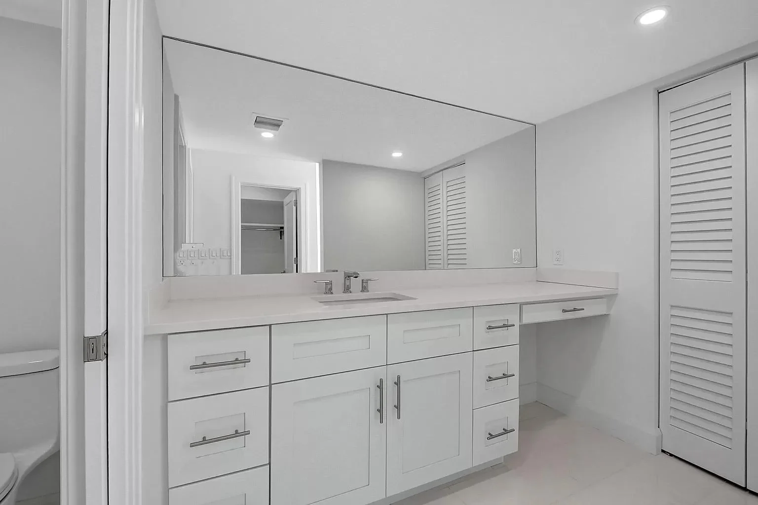 White bathroom vanity with quartz countertop, frameless mirror, and chrome fixtures