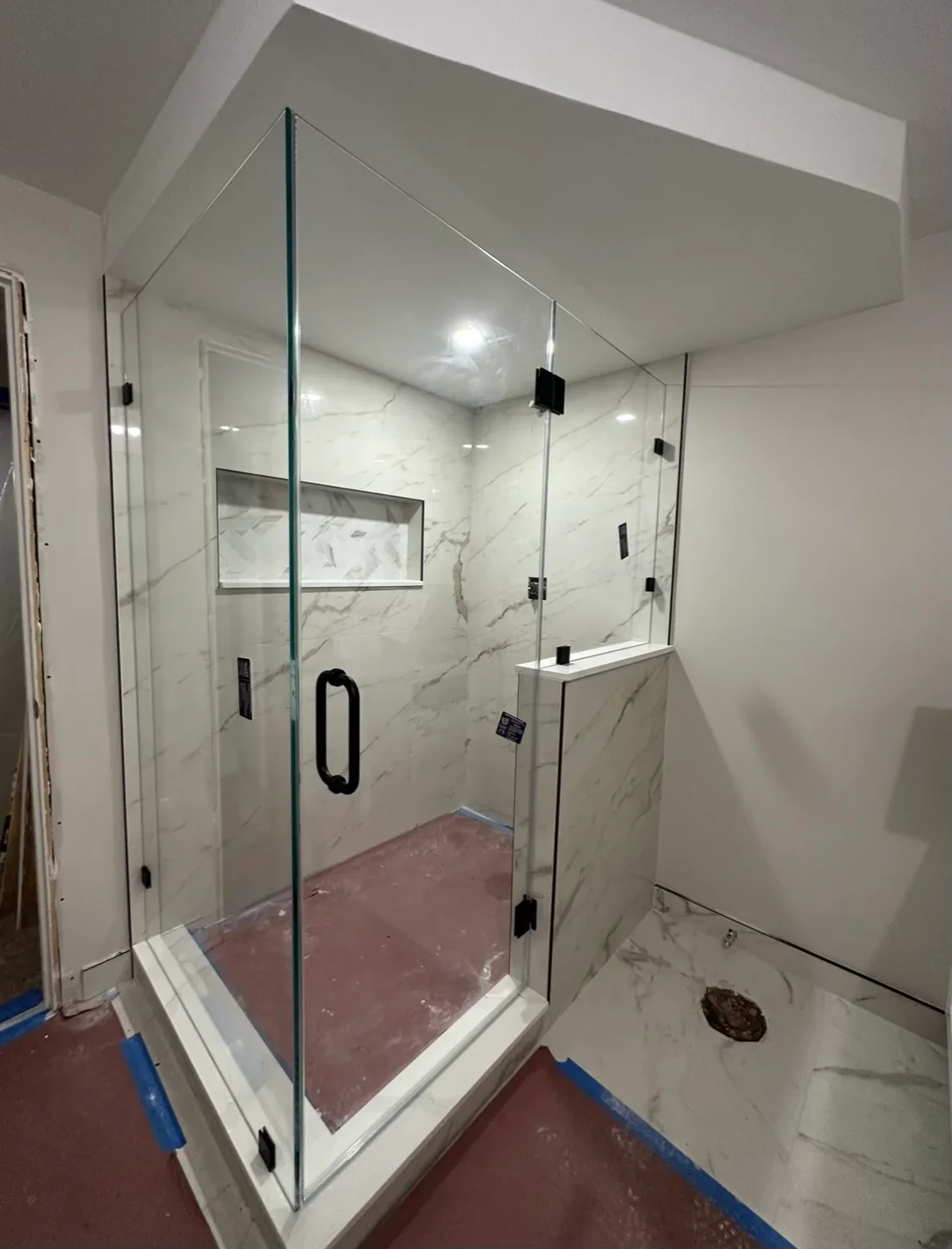 Frameless glass shower with marble tile walls, black hardware, and recessed lighting