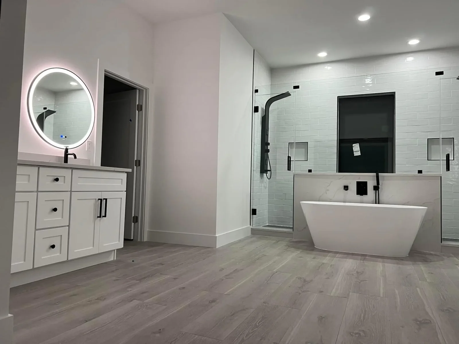 Modern bathroom with white vanity, LED mirror, freestanding tub, and tiled walk-in shower with black accents