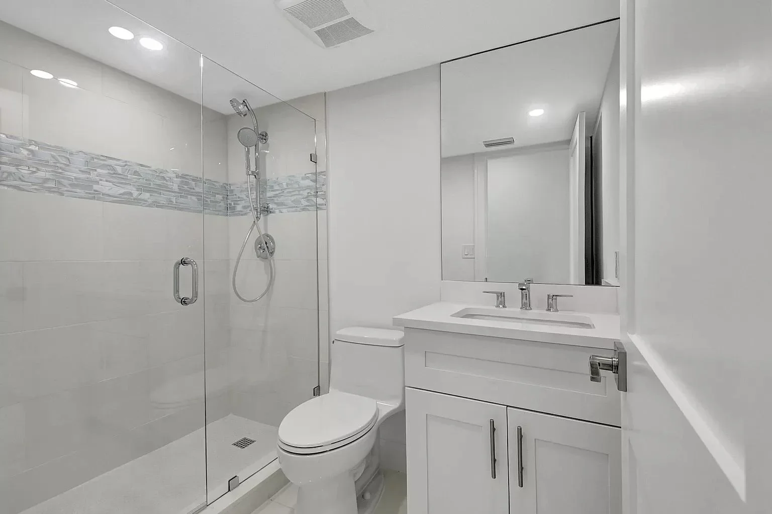 White subway tile bathroom with glass shower enclosure, white vanity, and mosaic accent tile