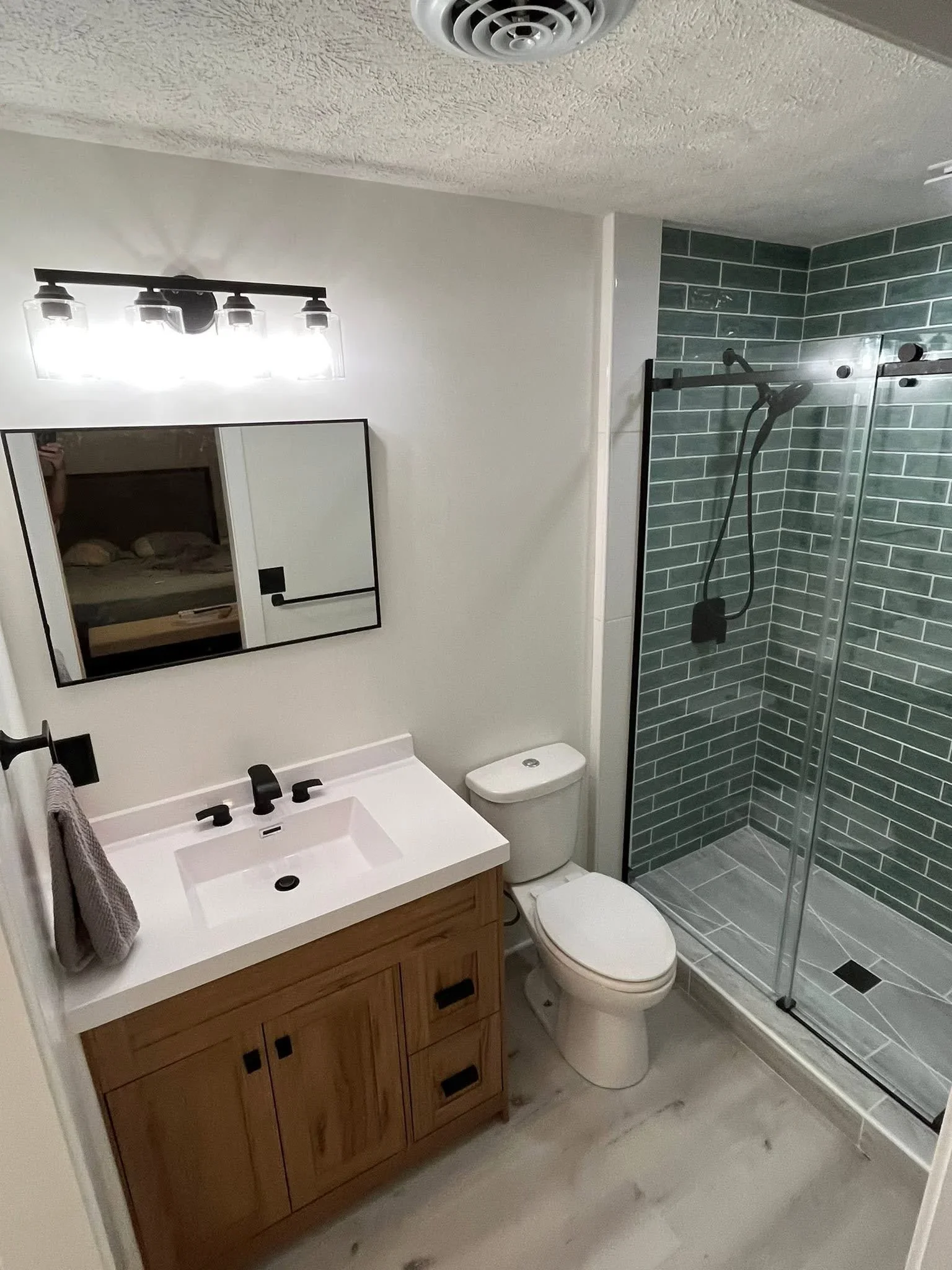 Bathroom with green subway tile shower, white quartz countertop, wood vanity, and frameless glass enclosure