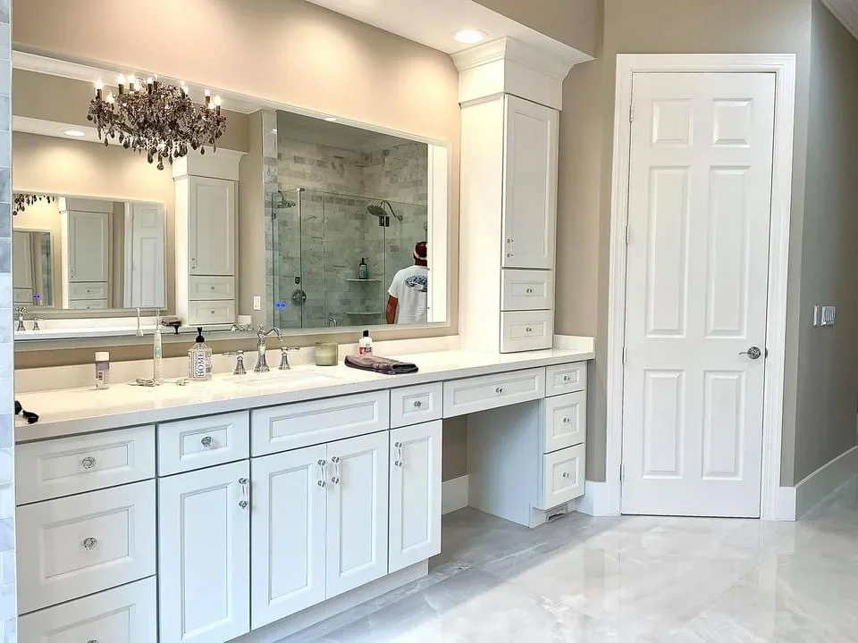 White vanity cabinetry with quartz countertop, dual sinks, marble tile shower with glass enclosure
