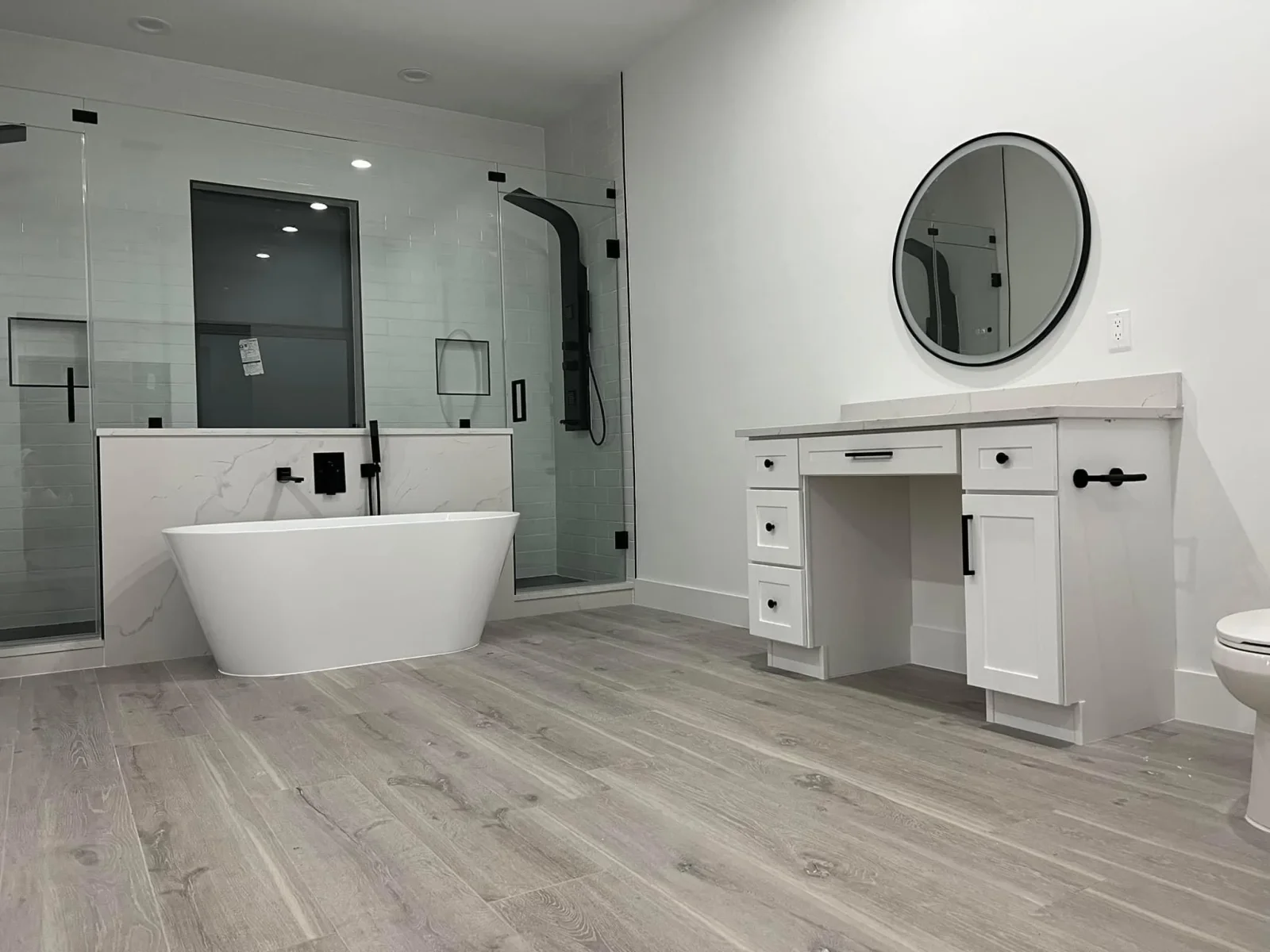 Modern bathroom with freestanding tub, white vanity, frameless shower, and gray wood-look flooring