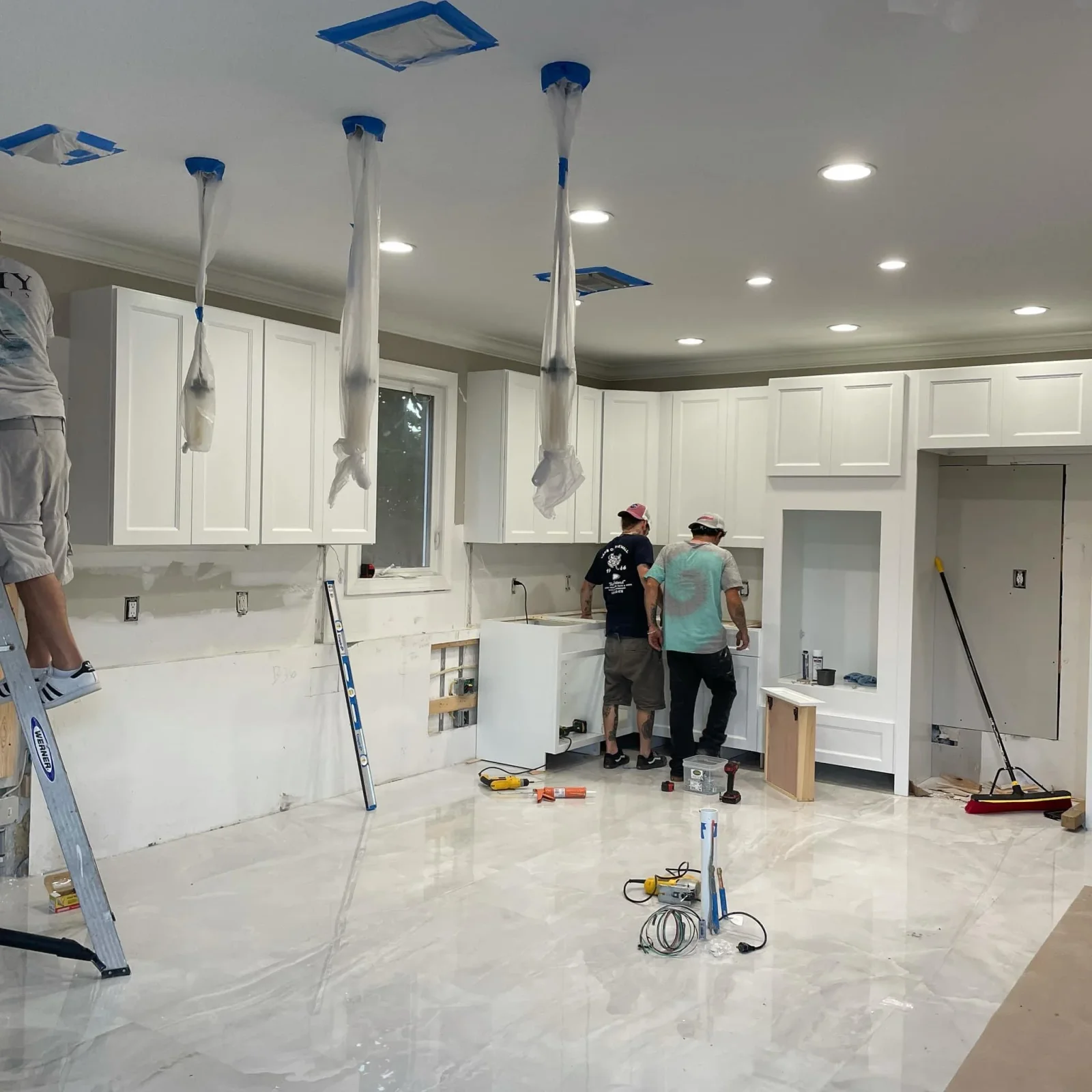 Kitchen remodel in progress with white cabinetry, quartz counters, recessed lighting, and island installation